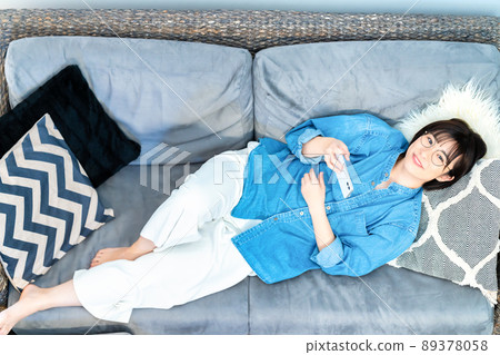 A woman with glasses lying on the sofa and watching a smartphone video A woman with glasses lying on the sofa and watching a smartphone video 89378058