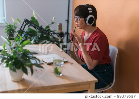 Portrait of mature woman wearing headphones and talking at online radio station - podcast and broadcast concept 89379587