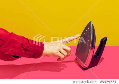 Colorful bright image of male finger touching retro iron isolated over pink yellow background 89379773