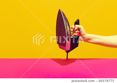 Colorful bright image of female hand holding retro iron isolated over pink yellow background 89379775
