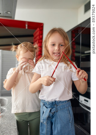 Two little girls siblings having fun and eating on the kitchen at home with japanese food. Two little girls siblings having fun and eating on the kitchen at home with japanese food. 89379824