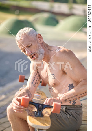 A man sitting and fixing details of his skateboard A man sitting and fixing details of his skateboard 89382451