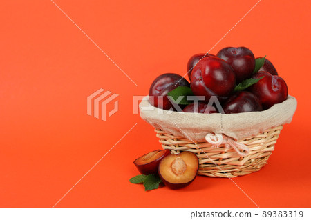 Wicker bowl with plums on an orange background 89383319