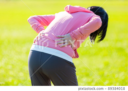 A middle-aged woman holding her back injured while exercising A middle-aged woman holding her back injured while exercising 89384018