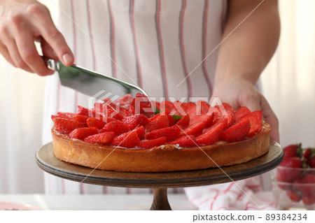 Woman in apron cut the strawberry tart Woman in apron cut the strawberry tart 89384234