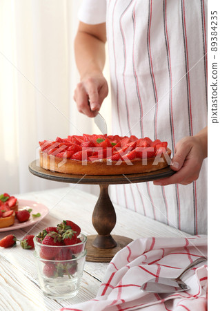 Woman in apron cut the strawberry tart Woman in apron cut the strawberry tart 89384235