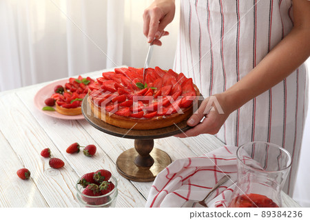 Woman in apron cut the strawberry tart Woman in apron cut the strawberry tart 89384236