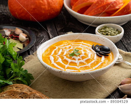 Funny food for Halloween. Pumpkin puree soup, spider web, dark old wooden table, side view. 89384529