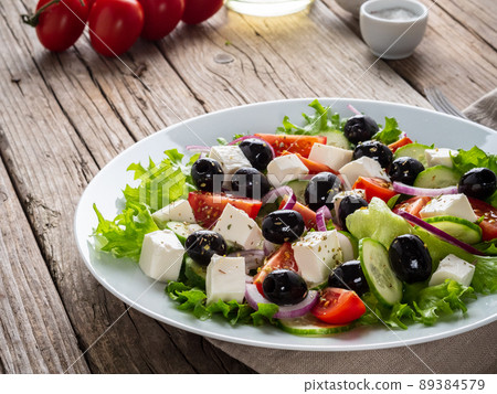 Greek salad on white plate on old rustic wooden table, side view Greek salad on white plate on old rustic wooden table, side view 89384579