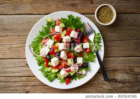 Greek salad on white plate on old rustic wooden table, top view Greek salad on white plate on old rustic wooden table, top view 89384590