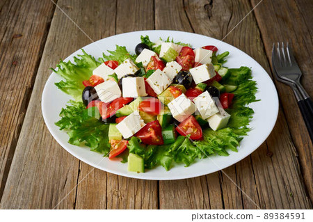 Greek salad on white plate on old rustic wooden table, side view 89384591