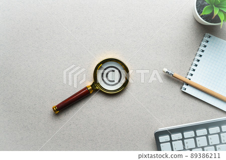 The concept of copyright and intellectual property. Magnifier with icon on the table. The concept of copyright and intellectual property. Magnifier with icon on the table. 89386211