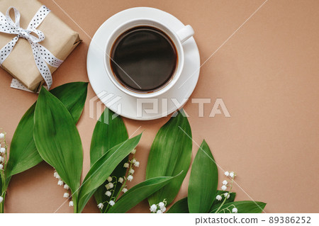 Cup of coffee ,gift and flowers lily of the valley on beige background top view. Flat lay. 89386252