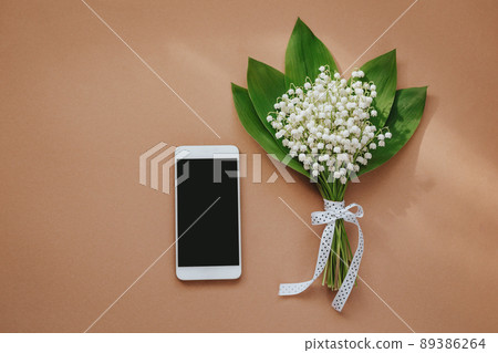 bouquet of lilies of the valley and phone space for text on beige background 89386264