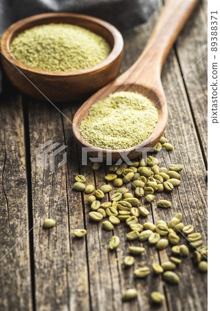 Ground green coffee in wooden spoon and unroasted coffee beans. 89388371