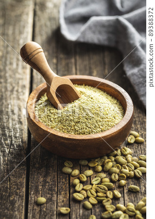 Ground green coffee in a wooden bowl and unroasted coffee beans. 89388372