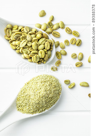 Ground green coffee and unroasted coffee beans on white table. Ground green coffee and unroasted coffee beans on white table. 89388378