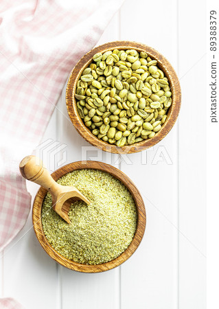 Ground green coffee and unroasted coffee beans on white table. 89388379