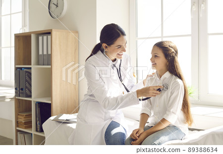 Happy child smiling while doctor is examining her lungs or heart during medical checkup 89388634