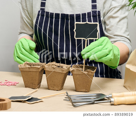A woman arranges wooden markers in paper cups with soil to sign the names of the planted seeds. Growing at home 89389019
