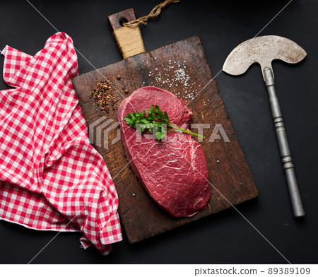 Raw beef tenderloin lies on a cutting board and spices for cooking on a black table 89389109
