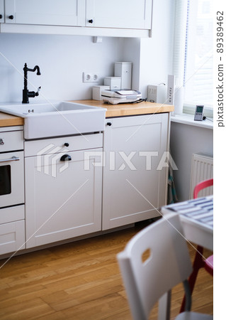 The interior of a kitchen in white tones with a sink, sandwich maker, stove, oven, dining table and a light window The interior of a kitchen in white tones with a sink, sandwich maker, stove, oven, dining table and a light window 89389462