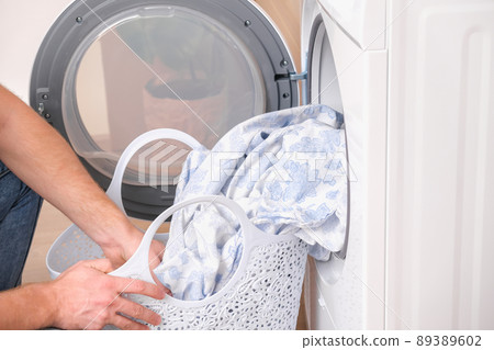 A man takes dried bed linen out of the dryer A man takes dried bed linen out of the dryer 89389602