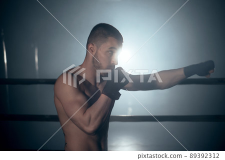 Muscular MMA fighter practicing punch, fight club concept. Muscular MMA fighter practicing punch, fight club concept. 89392312