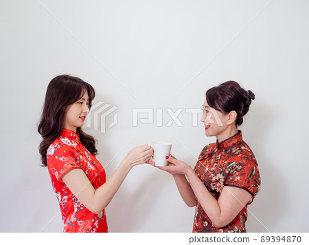 Portrait of mature asian mother and her asian daughter both wearing traditional cheongsam qipao dress relaxing drinking on white background. Portrait of mature asian mother and her asian daughter both wearing traditional cheongsam qipao dress relaxing drinking on white background. 89394870