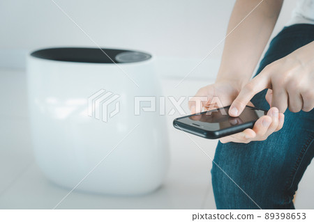 Woman control a modern air purifier through the application on a smartphone, a smartphone screen isolated in white color. Modern and smart home connectivity technology concept. 89398653