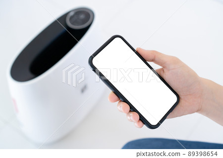 Woman control a modern air purifier through the application on a smartphone, a smartphone screen isolated in white color. Modern and smart home connectivity technology concept. Woman control a modern air purifier through the application on a smartphone, a smartphone screen isolated in white color. Modern and smart home connectivity technology concept. 89398654