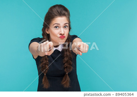 Closeup portrait of crazy woman pointing finger at camera. Studio shot, blue background Closeup portrait of crazy woman pointing finger at camera. Studio shot, blue background 89405364