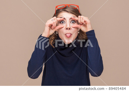 Crazy woman looking at camera and tongue out. Studio shot, light brown background 89405484