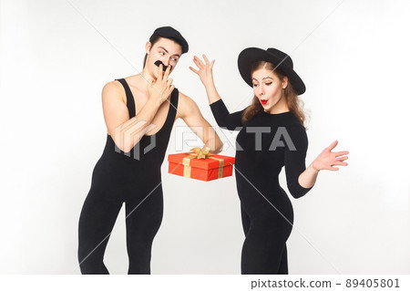 Man with fake mustache present gift box shocked woman. Studio shot, isolated on white background Man with fake mustache present gift box shocked woman. Studio shot, isolated on white background 89405801