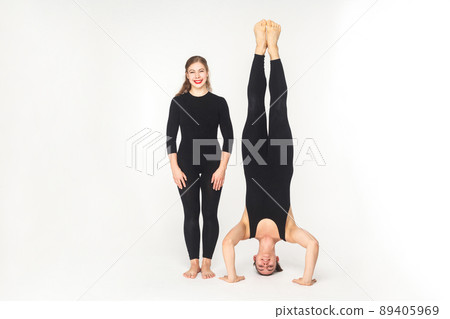 Woman toothy smile, standing near man stand on head. Studio shot, isolated on white background Woman toothy smile, standing near man stand on head. Studio shot, isolated on white background 89405969