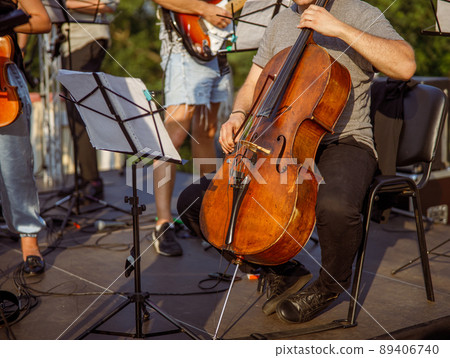 Male cellist playing violoncello in orchestra outdoors Male cellist playing violoncello in orchestra outdoors 89406740