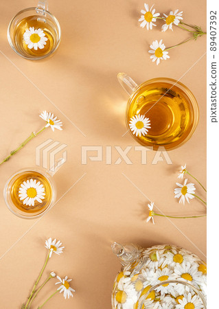 Chamomile tea. Cups of herbal tea, transparent teapot with camomile flowers on brown background. Calming drink concept. Trendy still life 89407392