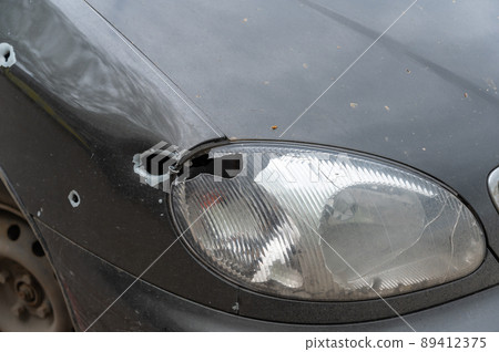 The front of the shot car. A sedan with a broken headlight by a bullet or shrapnel. Firing on civilians during the war between Russia and Ukraine in 2022. War crimes concept. The front of the shot car. A sedan with a broken headlight by a bullet or shrapnel. Firing on civilians during the war between Russia and Ukraine in 2022. War crimes concept. 89412375
