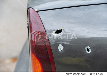 Close-up of the rear of the shelled car. Sedan with through holes from shrapnel. The war in Ukraine 2022. Russian aggression. The shelling of civilians. War crimes concept Close-up of the rear of the shelled car. Sedan with through holes from shrapnel. The war in Ukraine 2022. Russian aggression. The shelling of civilians. War crimes concept 89412380