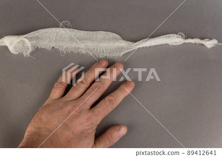 The hand of a mature man and a piece of white bandage against a gray background. Health and Medicine. Angled view from above. 89412641