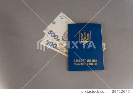 A blue covered passport and cash against a gray background. Ukrainian ID card and hryvnias. 89412643