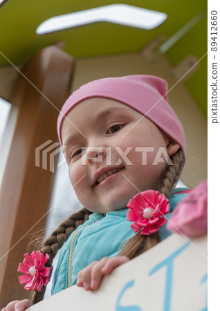 Portrait of a preschool child on the playground. Five-year-old girl in a pink hat and long pigtails. Bottom-up view. Portrait of a preschool child on the playground. Five-year-old girl in a pink hat and long pigtails. Bottom-up view. 89412660