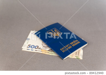 A blue covered passport and cash against a gray background. Ukrainian ID card and hryvnias. A blue covered passport and cash against a gray background. Ukrainian ID card and hryvnias. 89412940
