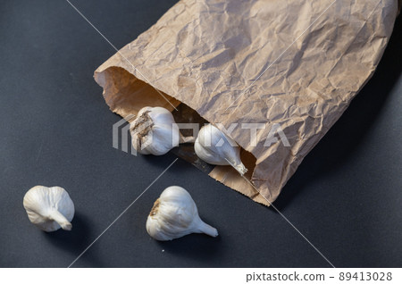 Brown paper bag with garlic against a black background. Heads of ripe garlic in the peel. Close-up. Selective focus Brown paper bag with garlic against a black background. Heads of ripe garlic in the peel. Close-up. Selective focus 89413028