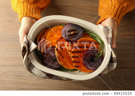 Female hands hold baking tray with baked pumpkin on wooden background 89415010