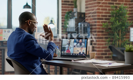 Young businessman attending teleconference meeting on laptop, talking to colleagues on online videocall conference. Chatting on videoconference for remote telecommunication with headphones. Young businessman attending teleconference meeting on laptop, talking to colleagues on online videocall conference. Chatting on videoconference for remote telecommunication with headphones. 89415993