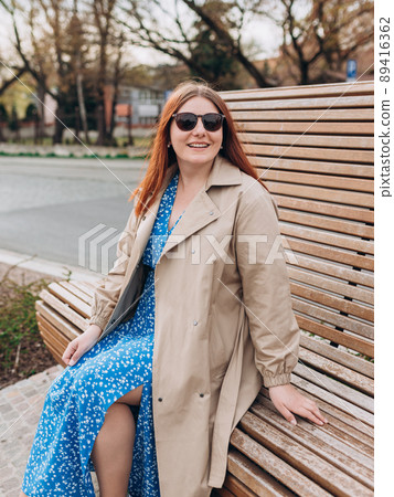 Happy cheerful young woman siting on the bench in the park on city street, Urban lifestyle concept. Traveler. Portrait of beautiful girl in sunglasses smiling outdoors. Happy cheerful young woman siting on the bench in the park on city street, Urban lifestyle concept. Traveler. Portrait of beautiful girl in sunglasses smiling outdoors. 89416362