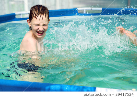Happy boy splashing on summer pool having fun leisure activity 89417524