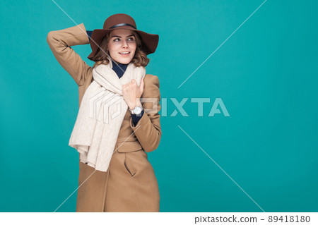 Happy smiling girl dressed in autumn coat, hat and scarf. Studio shot, isolated on blue background 89418180