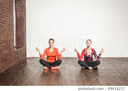 Yoga concept. Two cute woman sit in lotus pose and meditating. Studio shot 89418251